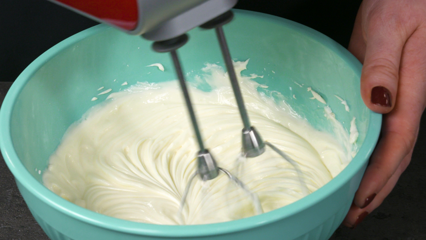 Die Creme für den Eierlikör Drip Cake mit weißer Schokolade wird in einer Schüssel mit einem Handmixer verrührt.