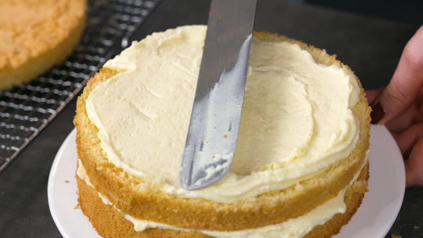 Boden und Creme werden für den Eierlikör Drip Cake mit weißer Schokolade gestapelt und bestrichen.