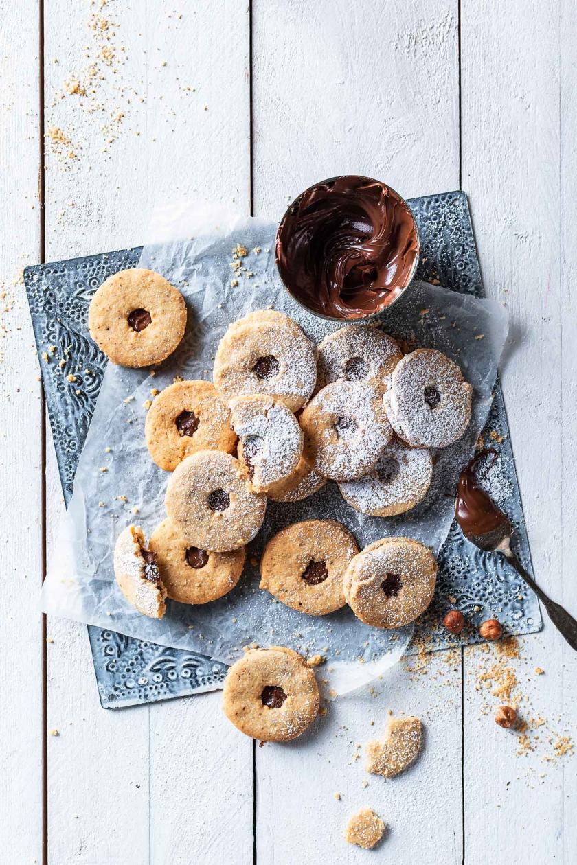 Mehrere Eigelb-Plätzchen mit Nutellafüllung und Puderzucker auf eine Stück Backpapier.