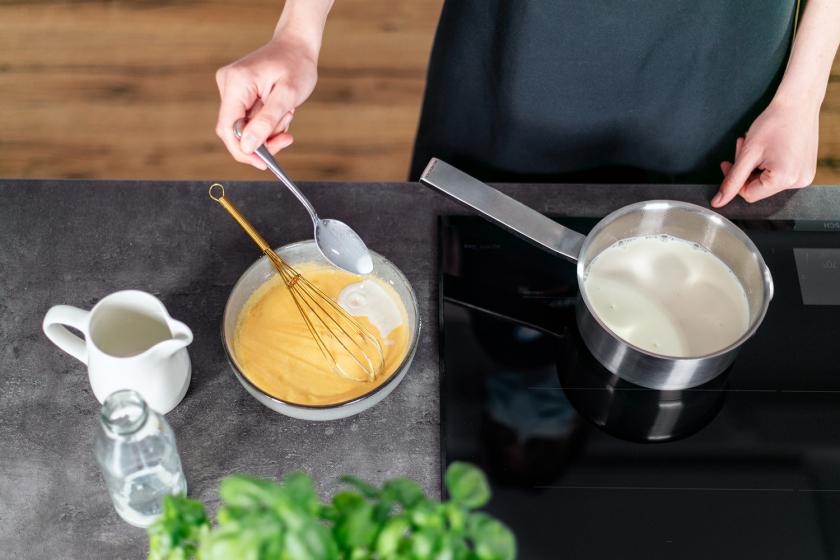 Heiße Milch wird zur Eimasse in eine Schüssel gelöffelt.