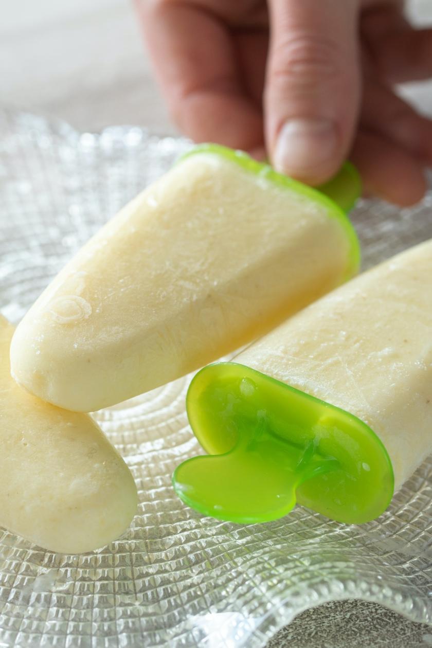 Eis am Stiel mit Ananas und Mango wird von einem Teller aufgenommen.