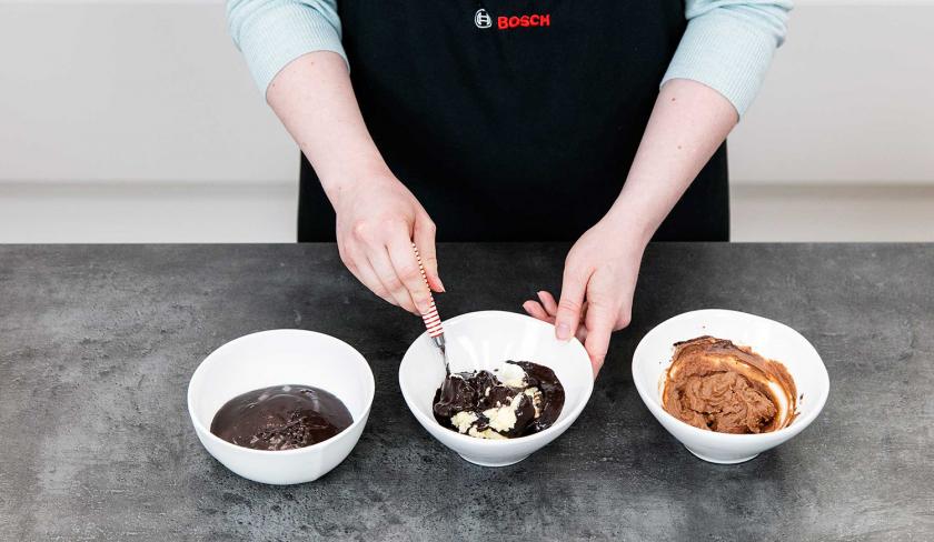 Für die Dekoration der Eiskaffee-Torte wird Frosting mit der Kaffeecreme in drei Schüsselchen in verschiedene Brauntöne eingefärbt.