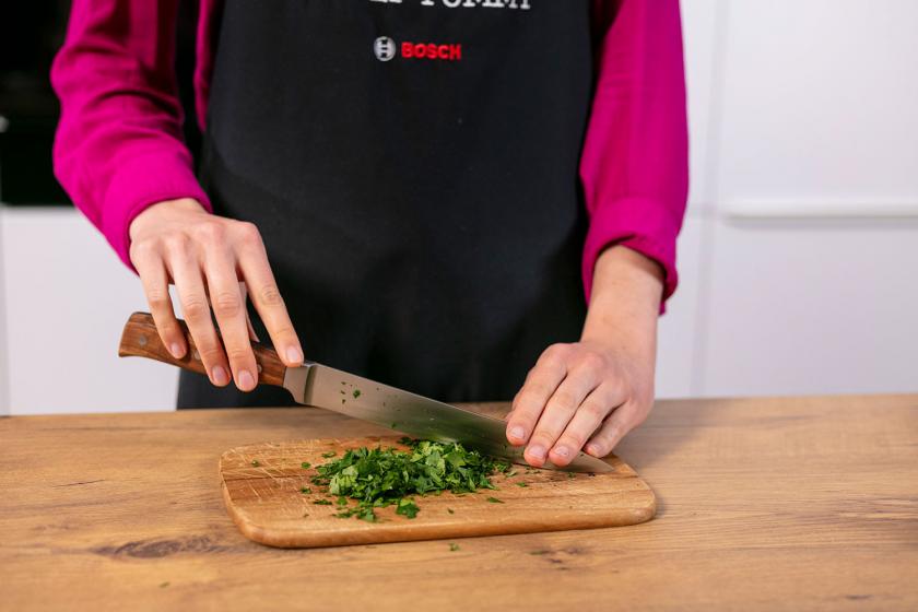 Petersilie wird auf einem Holzbrett gehackt.