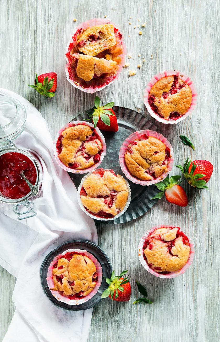 Mehrere Erdbeer-Muffins stehen auf einem Tisch it Marmelade und Erdbeeren.