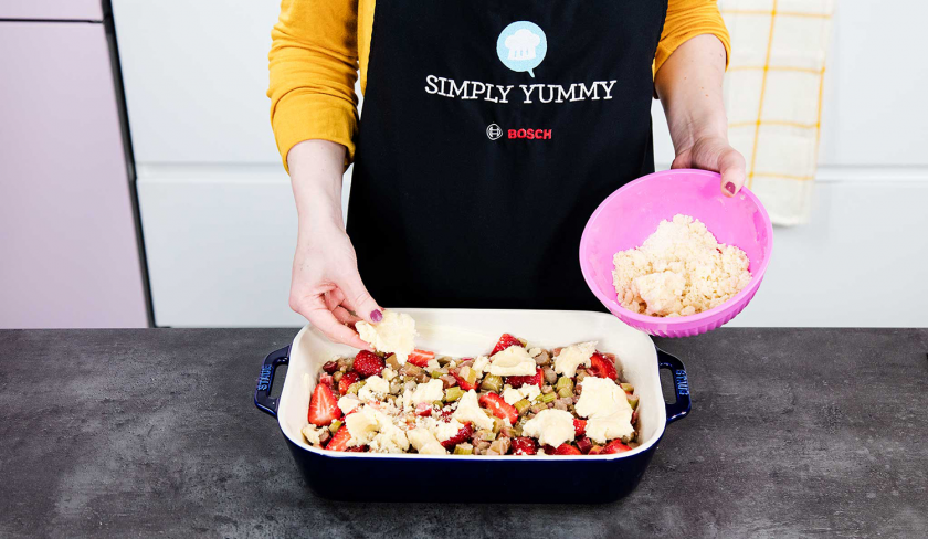 Streuselteig wird auf der Füllung für den Erdbeer-Rhabarber-Cobbler verteilt.