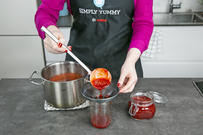 Die Erdbeermarmelade wird mit einer Kelle in Gläser gefüllt.