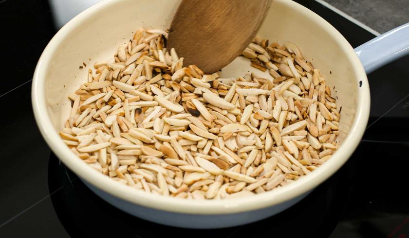 Für die Espresso-Muffins mit weißer Schokolade werden Mandelstifte in einer Pfanne geröstet.