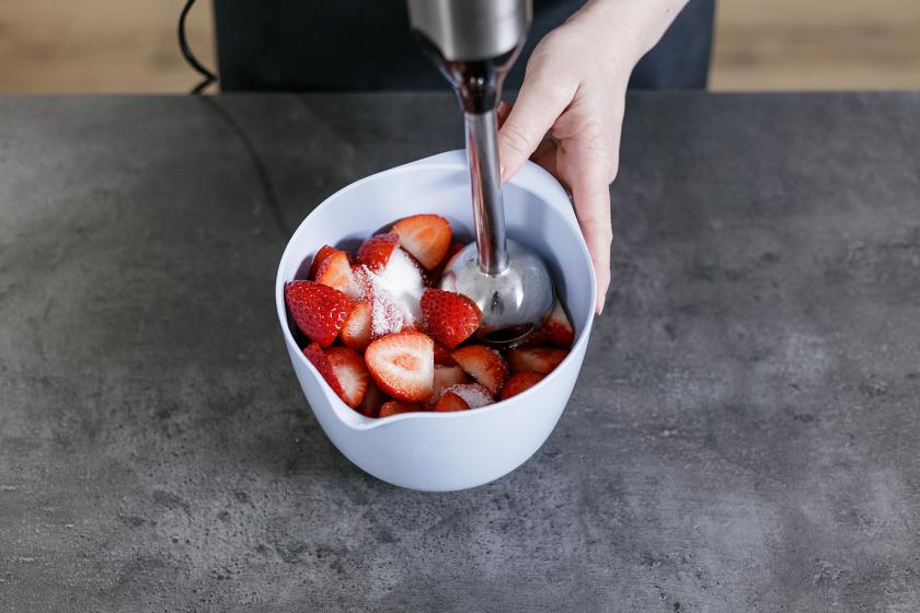 Erdbeeren werden mit Zucker in einer Rührschüssel püriert.