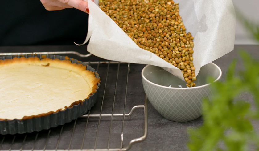 Die Erbsen vom Blindbacken werden vom Boden des fruchtiger Mosaik Kuchens genommen und in eine Schale gefüllt.