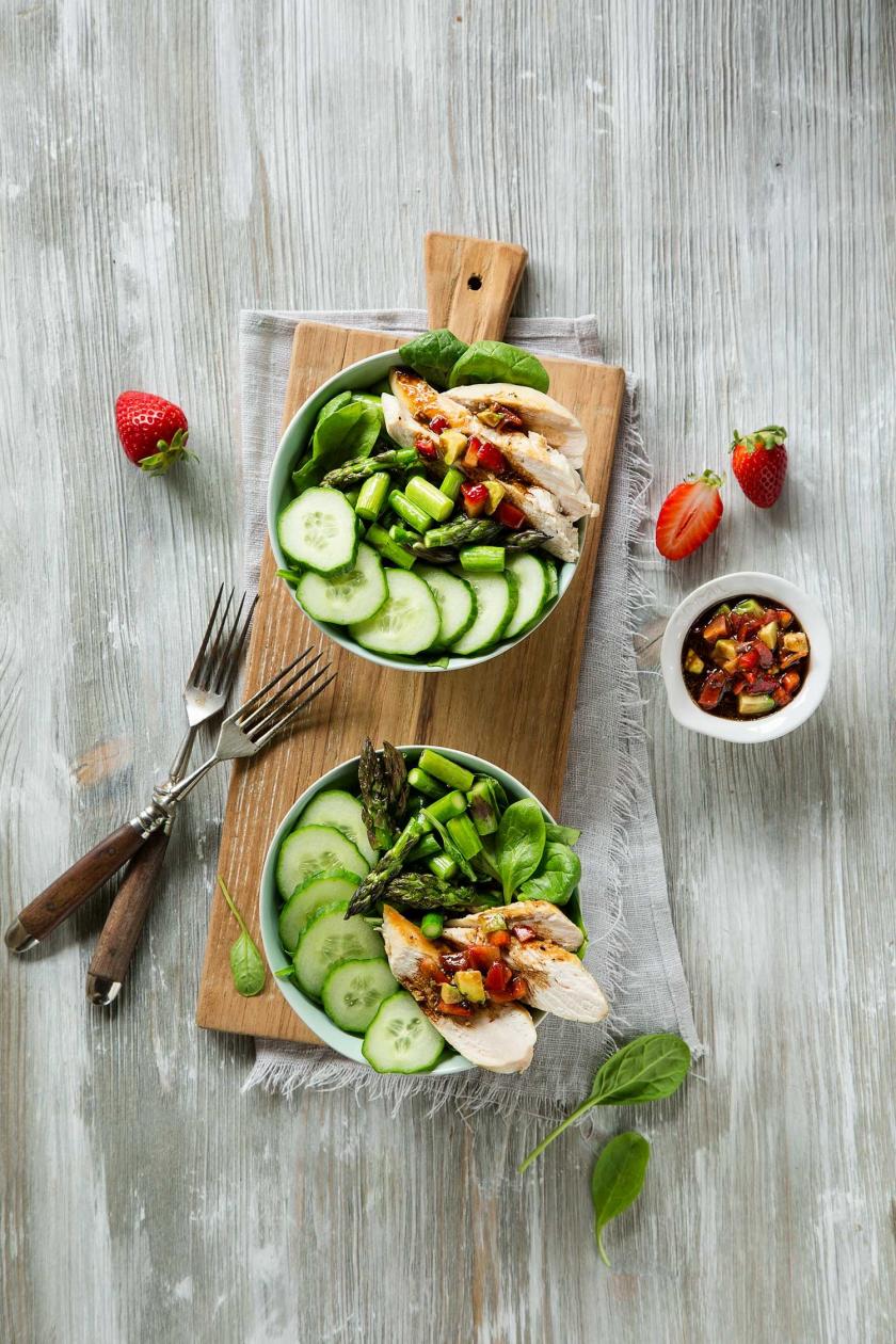 Zwei Frühlings Buddha Bowls stehen auf eine Holzbrett, daneben Salsa in einer kleinen Schale.