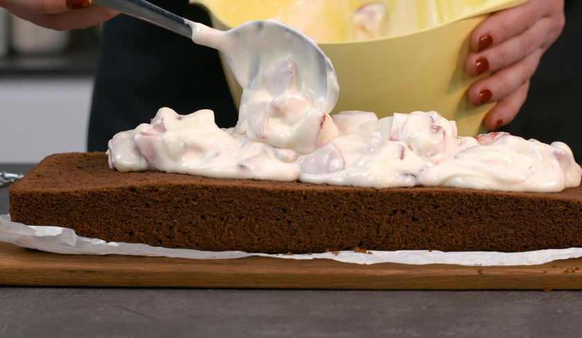 Die Füllung für gefüllter Schoko-Erdbeerkuchen wird auf einer Kuchenhälfte verteilt.