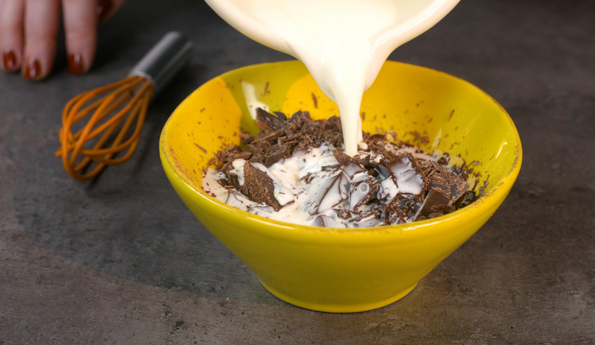 Sahne wird auf Schokolade geschüttet, um die Ganache für gefüllter Schoko-Erdbeerkuchen zuzubereiten.
