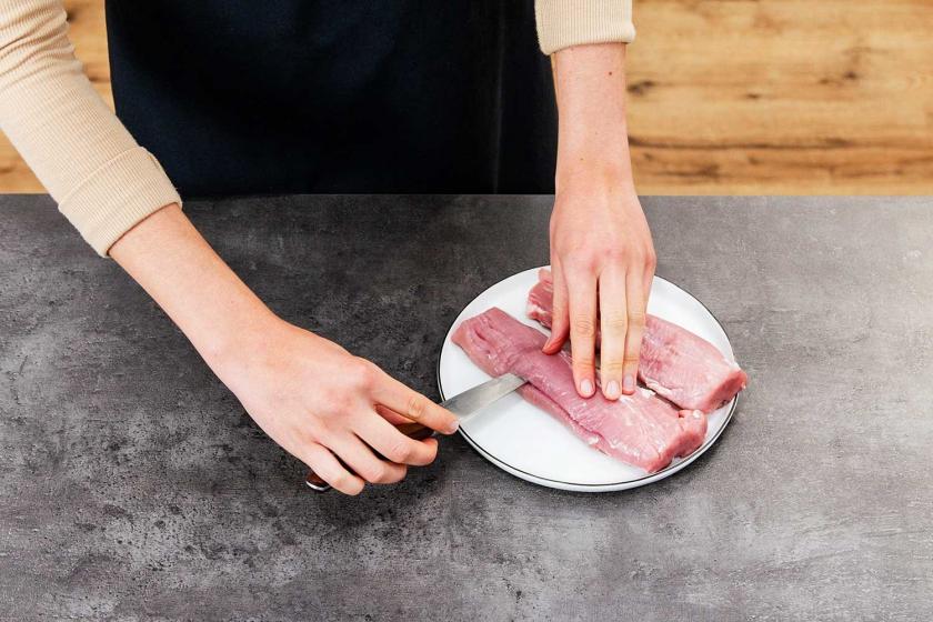Schweinefilet wird mit einem Messer längs eingeschnitten.