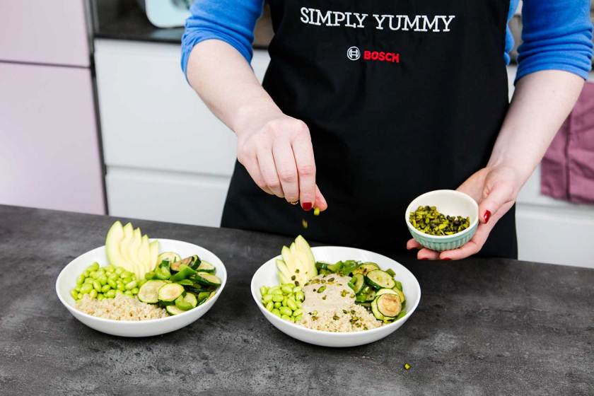 Die grüne Buddha Bowl wird angerichtet, jemand streut Pistazien über die Zutaten.