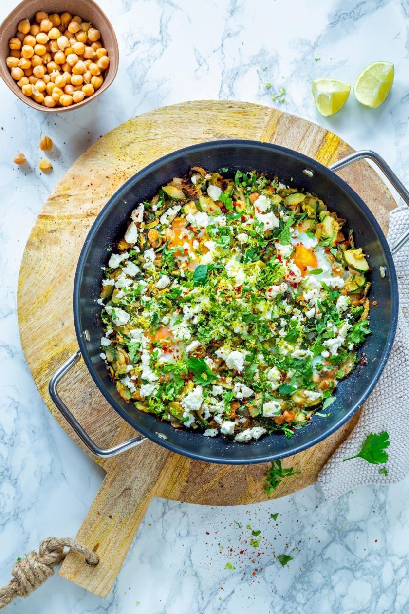Grünes Shakshuka mit Eiern, Feta und Minze in einer Pfanne auf einem Holzbrett.