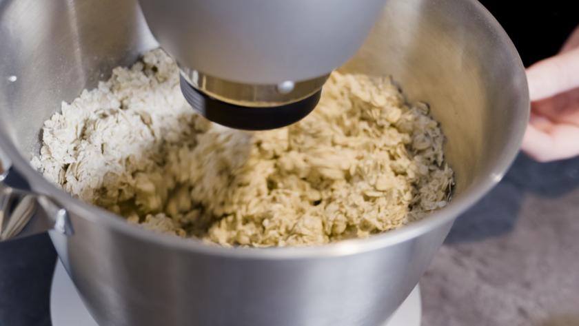 Haferflocken werden unter den Teig für das Haferflockenbrot mit Quark in der Rührschüssel untergerührt.