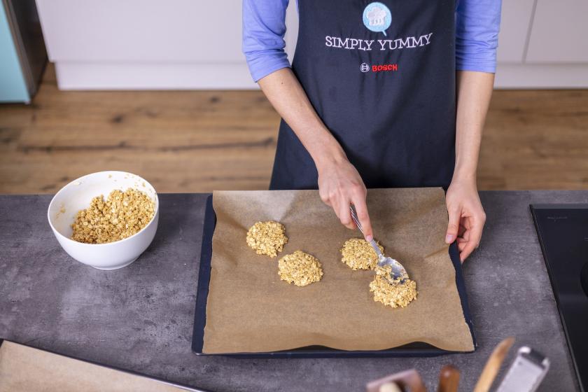 Der Teig für die Haferflockenkekse ohne Zucker wird mit einem Löffel auf das Backblech gegeben.