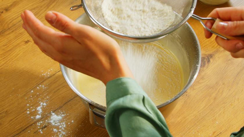 Mehl wird auf den Teig für die Himbeer-Quark-Torte gesiebt.