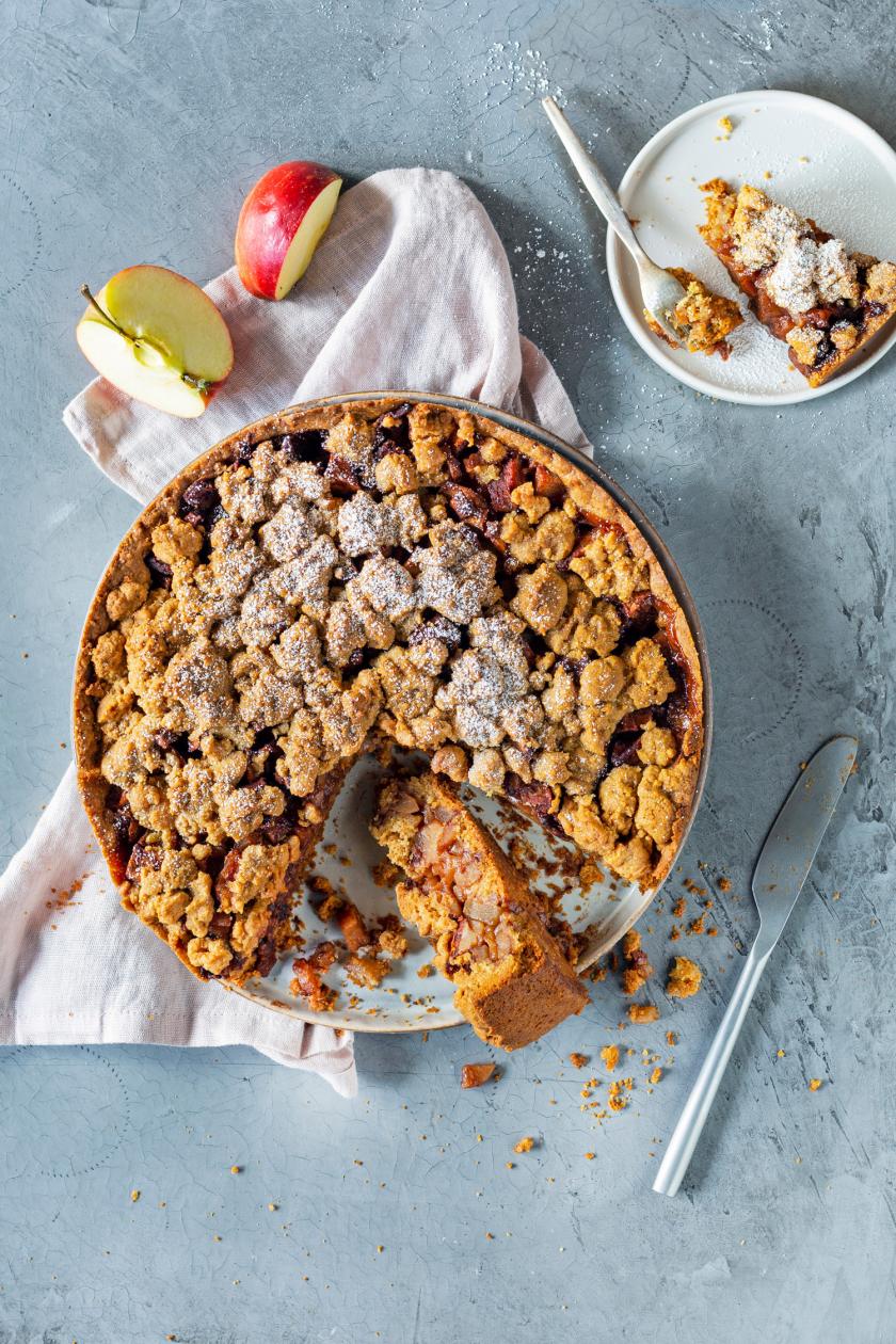 Holländischer Apfelkuchen angeschnitten auf einer Kuchenplatte mit angelegtem Messer.