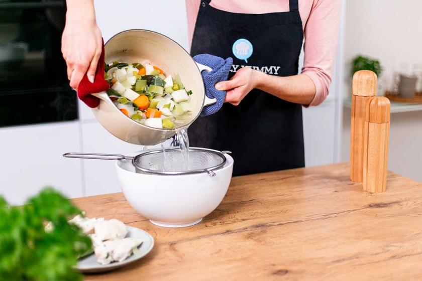 Hühnerbrühe wird durch ein Sieb abgeseiht.