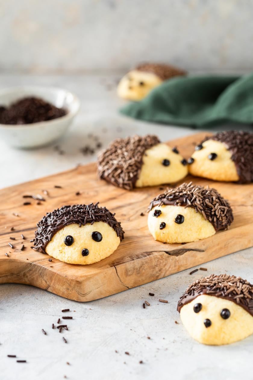 Igelkekse auf einem Holzbrett, daneben Zutaten wie Schokostreusel und Zuckerschrift