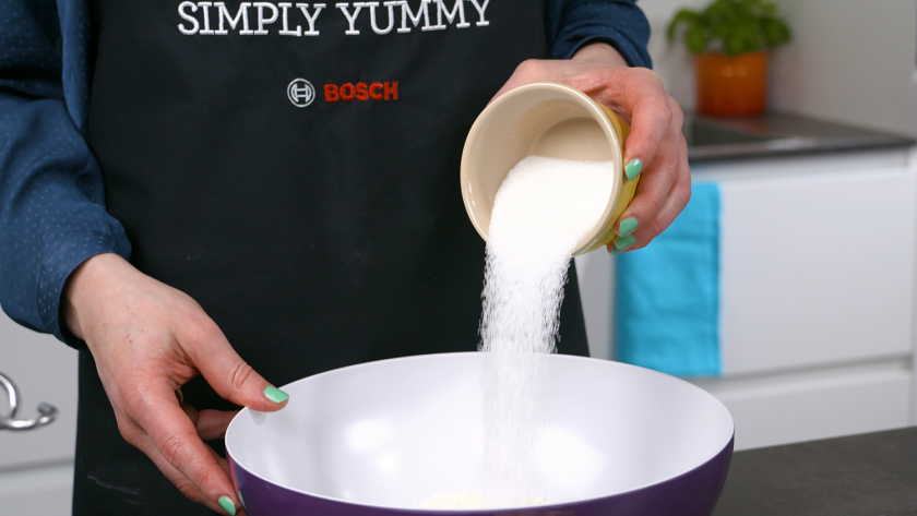 Für den Boden der Käsekuchenmuffins mit Streuseln wird Zucker in eine Schüssel geschüttet.