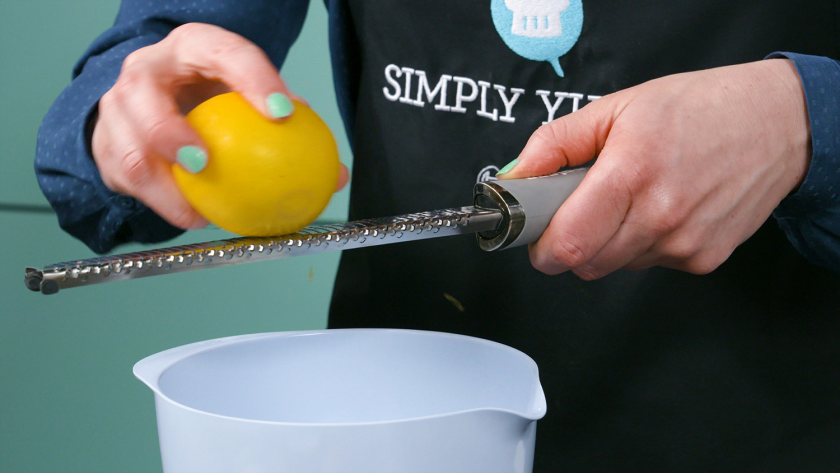 Jemand reibt Zitronenschale über einer Schüssel ab für die Füllung der Käsekuchenmuffins mit Streuseln.