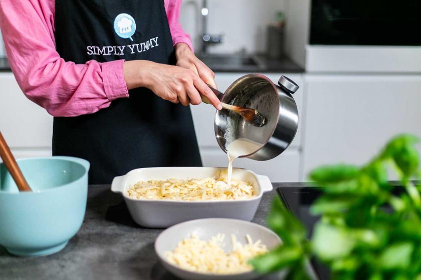 Spätzle in einer Auflaufform werden mit Sahne übergossen.