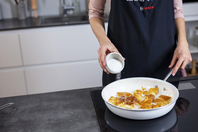 Kaiserschmarrn in einer Pfanne wird mit Zucker bestreut.