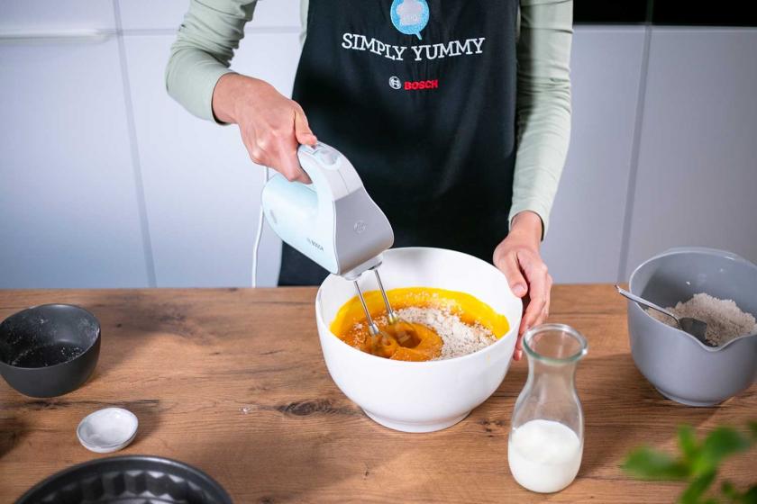 Der Teig für den Kürbiskuchen ohne Zucker wird in einer Rührschüssel mit einem Handmixer verrührt.
