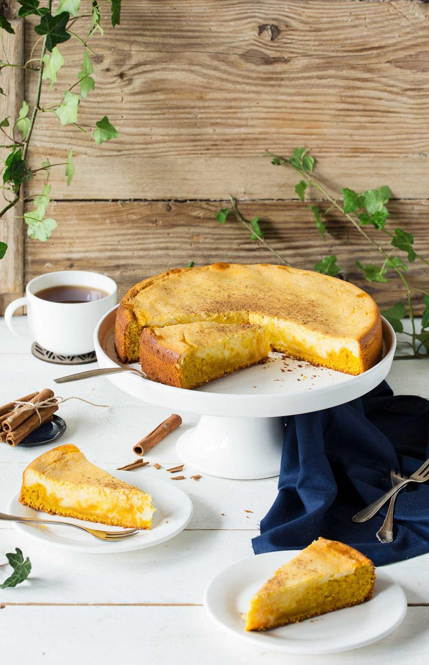 Kürbiskuchen mit Cheesecakeswirl angeschnitten auf einer Etagere auf einem gedeckten Tisch.
