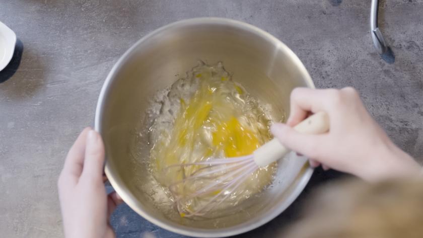 Eine Eimasse wird in einer Rührschüssel mit einem Schneebesen verquirlt.