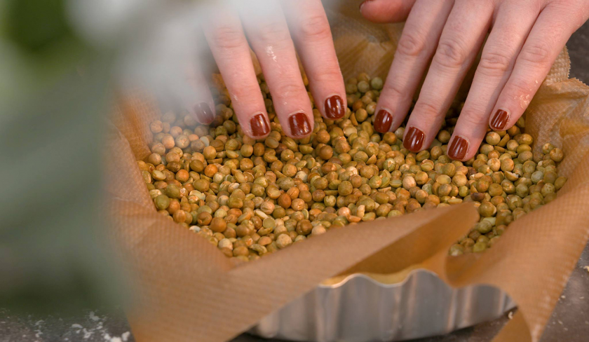 Der Boden der Lemon Curd Tarte mit Balsamico-Kirschen wird mit Backpapier und Backerbsen ausgekleidet.