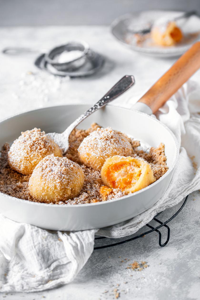 Marillenknödel mit Semmelbrösel und Puderzucker in einer Pfanne mit Löffel.