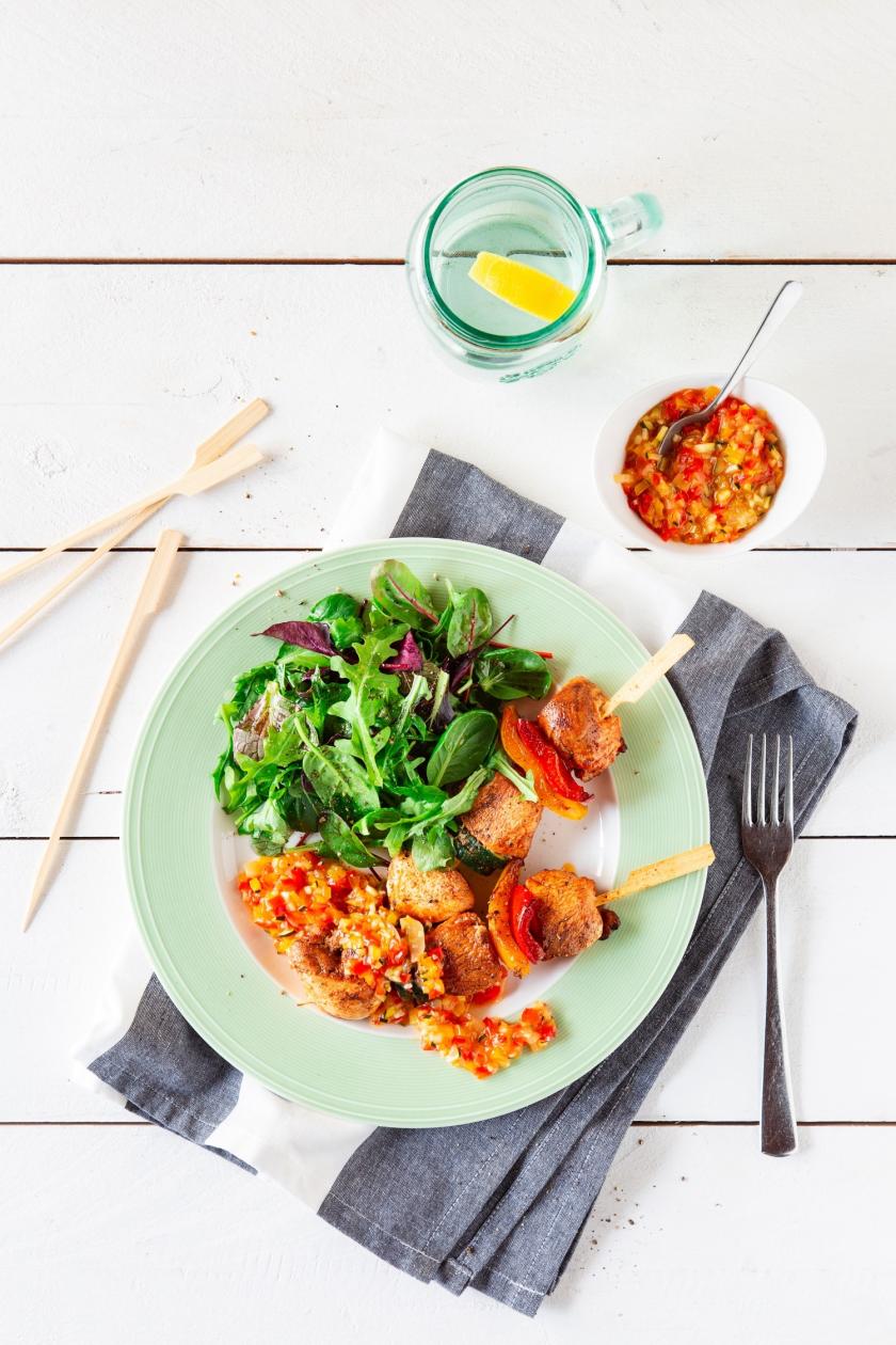 Hähnchenspieße mit Chutney und Salat auf Teller.