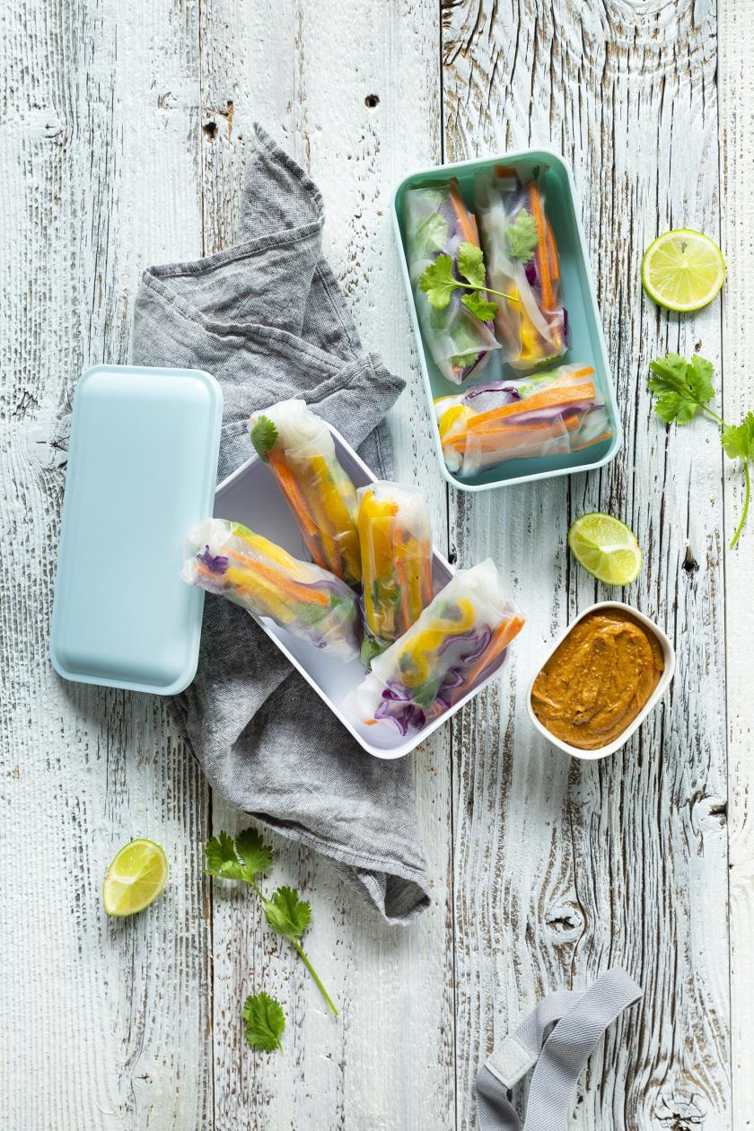Sommerrollen Meal Prep vegan liegen in einer blauen Lunchbox. Daneben ein Erdnussdip.