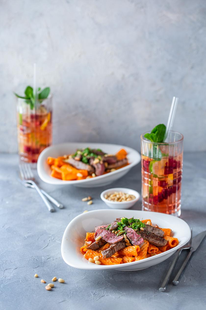 Nudeln mit Paprikasoße und Rinderfiletstreifen in einem tiefen Teller mit angelegtem Besteck.