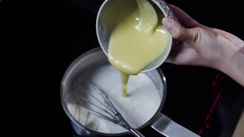 Eigelbmischung wird in die Milch in einem Topf eingerührt.