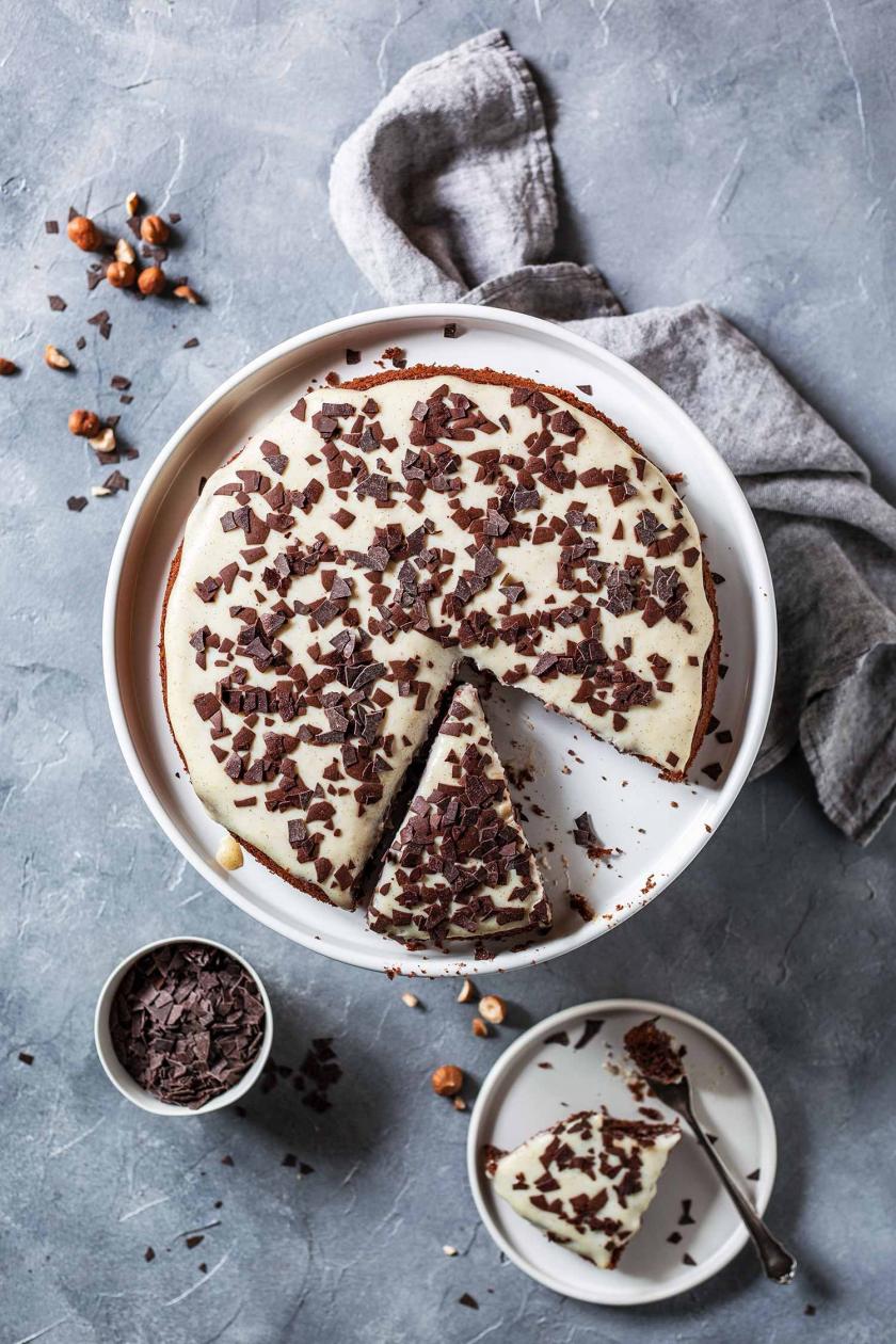 Nuss-Pudding-Kuchen mit Schokoraspeln angeschnitten auf einer Kuchenplatte.