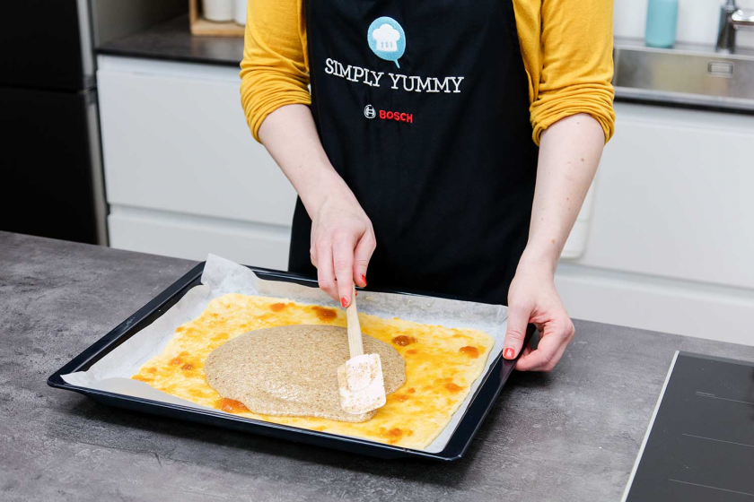 Die Nussmasse für die Nussecken wird auf der Aprikosenmarmelade verteilt.