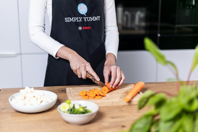 Möhren werden auf einem Holzbrett in Scheiben geschnitten.
