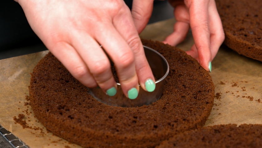 Jemand sticht ein Loch aus dem Biskuitboden für die Füllung des Piñata Kuchens.