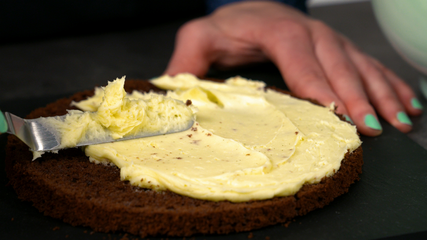 Ein Boden des Piñata Kuchens wird mit Buttercreme eingestrichen.