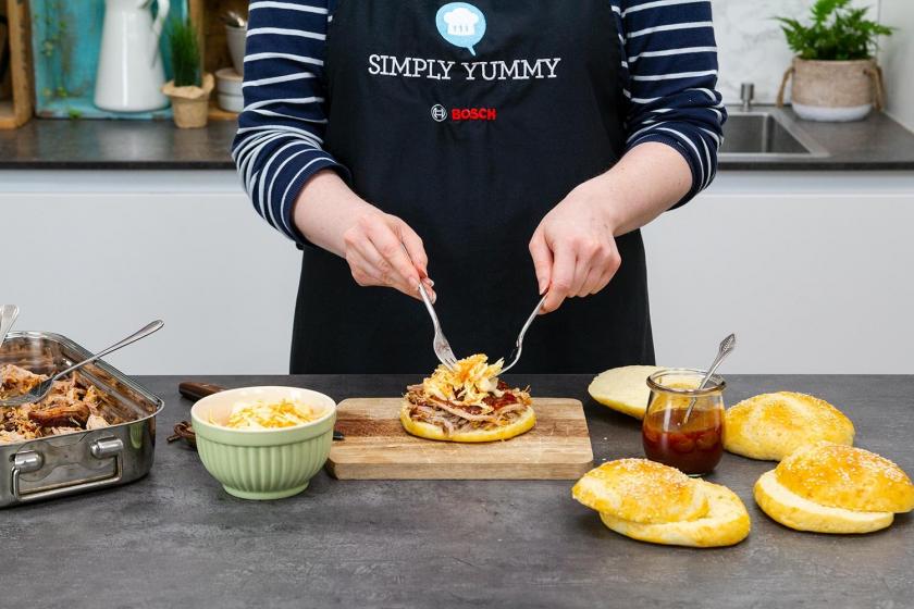 Der Pulled Pork Burger wird zusammengesetzt. Coleslaw wird auf das Pulled Pork gegeben.