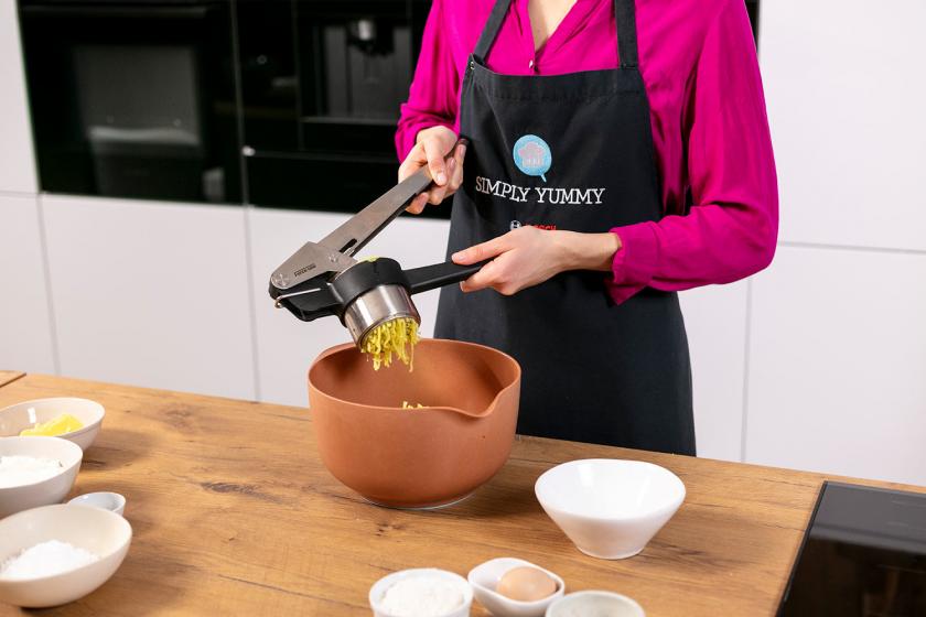 Für den Teig der Quarkkeulchen werden Kartoffeln durch eine Kartoffelpresse gedrückt.