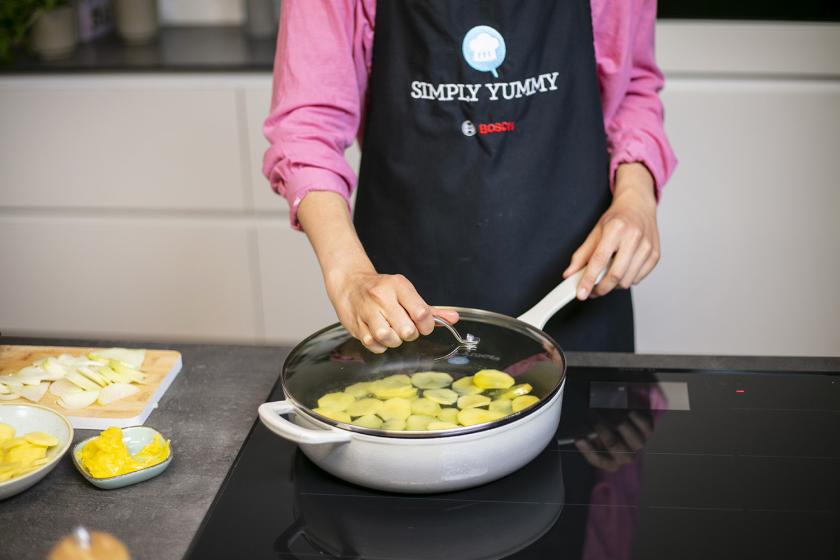 Ein Deckel wird auf die Pfanne mit Bratkartoffeln aus rohen Kartoffeln gegeben.