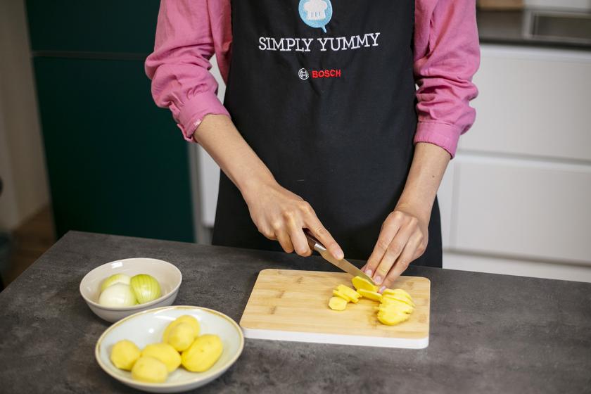 Kartoffeln werden auf einem Holzbrett in dünne Scheiben geschnitten.