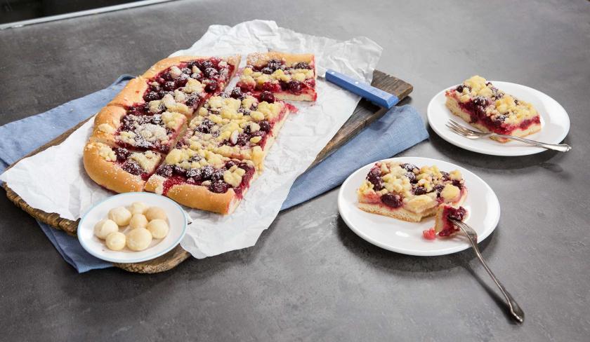Der Kirsch-Streuselkuchen ist auf zwei Tellern angerichtet. Daneben steht der angeschnittene Kuchen.