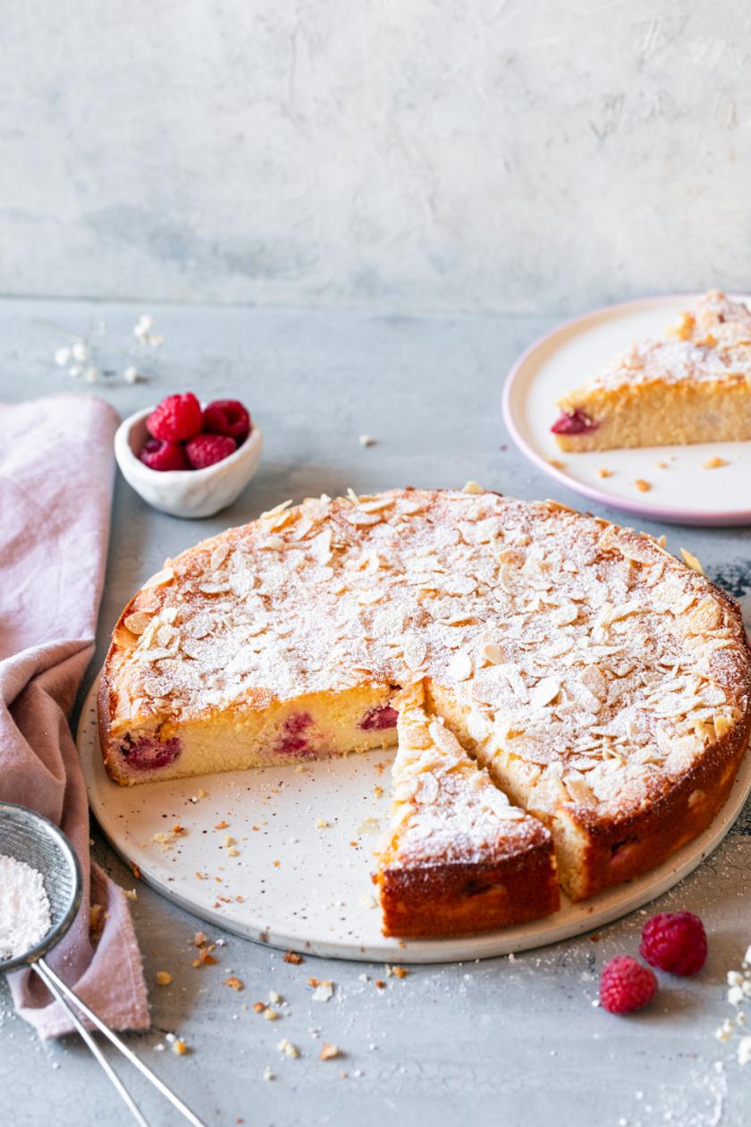 Ricottakuchen angeschnitten auf einer Kuchenplatte garniert mit Himbeeren