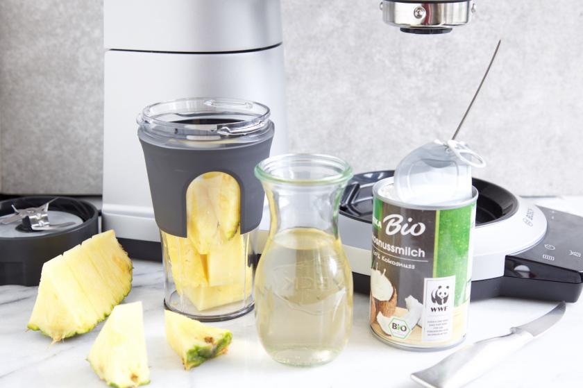 Ananas und Kokosmilch vor Hochleistungsmixer für Ananas-Smoothie